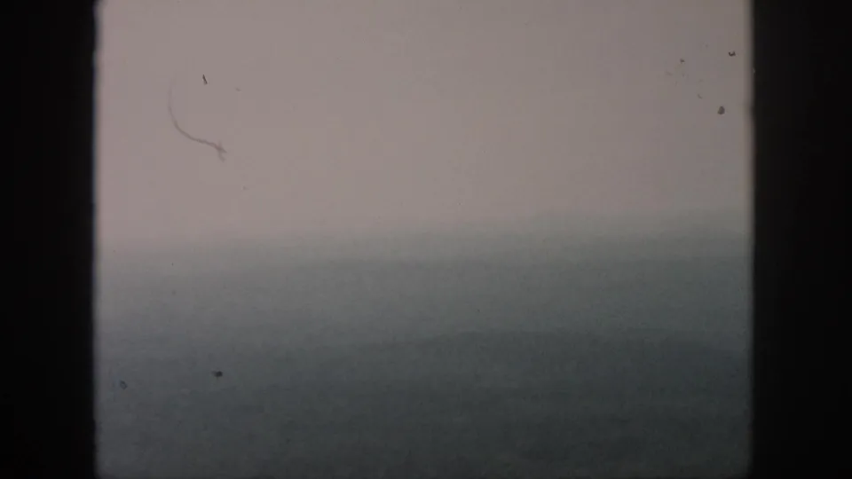 Soft 1958 8mm frame attributed to Dayton, Ohio, showing distant ridges and green terrain through haze from an aircraft window.