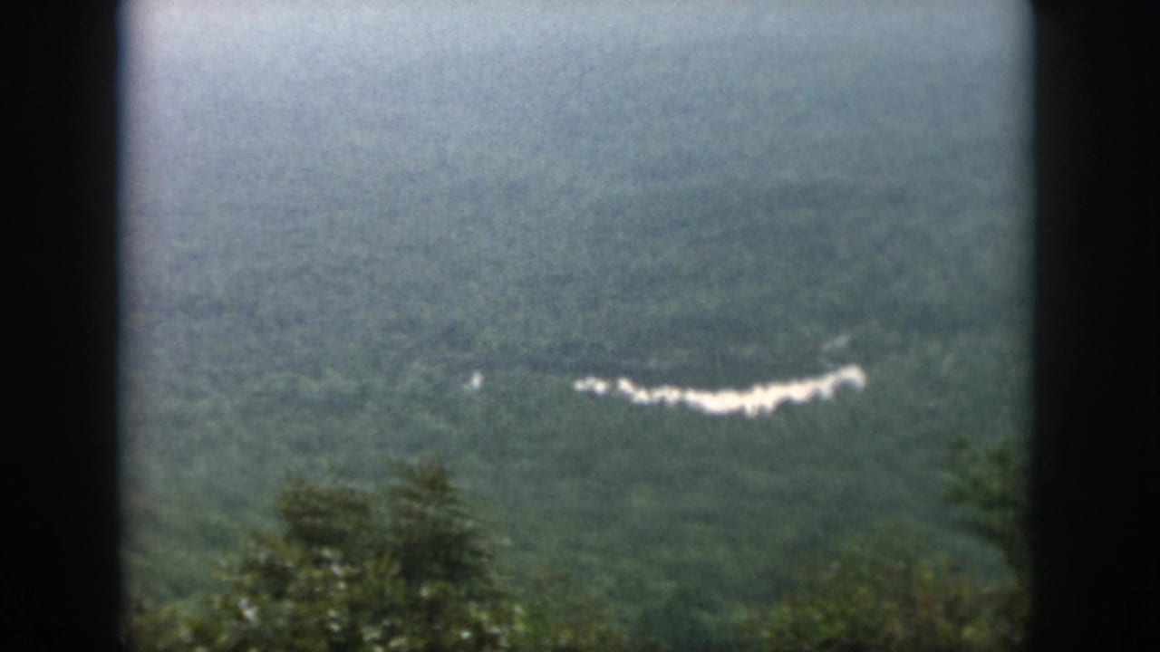 1958 Dayton-area home-movie frame of a soft, hazy forested valley with a pale winding line in the distance.