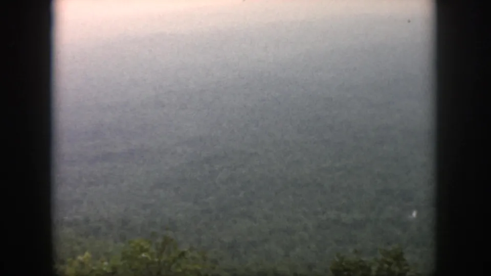1958 home-movie frame looking over a broad, misty green valley near Dayton, with no people or structures visible.