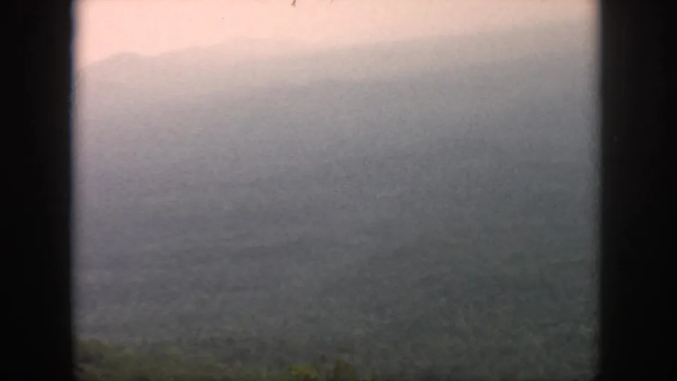 Hazy 1958 Dayton-area landscape frame with layered hills, forest canopy, and dark borders from the filming position.