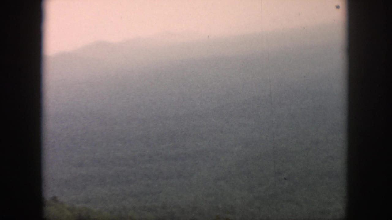 1958 8mm home-movie frame from the Dayton, Ohio metadata context showing misty hills through an airplane window.