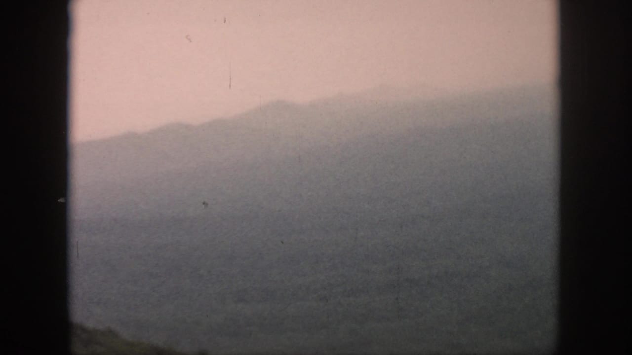 A muted 1958 aerial travel view shows layered hills and a valley through the aircraft window frame.