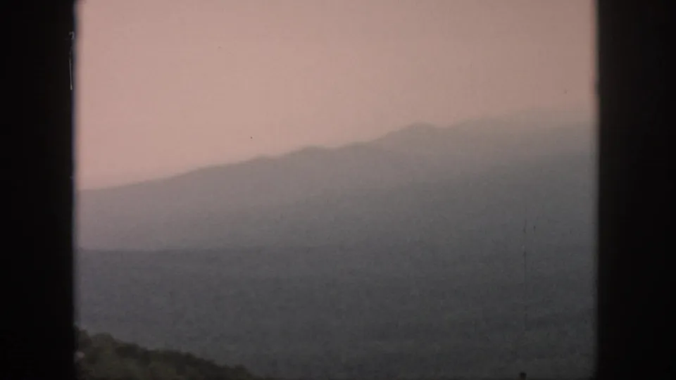 The frame holds a hazy, green ridge line and dark window border from 1958 8mm airplane travel footage.