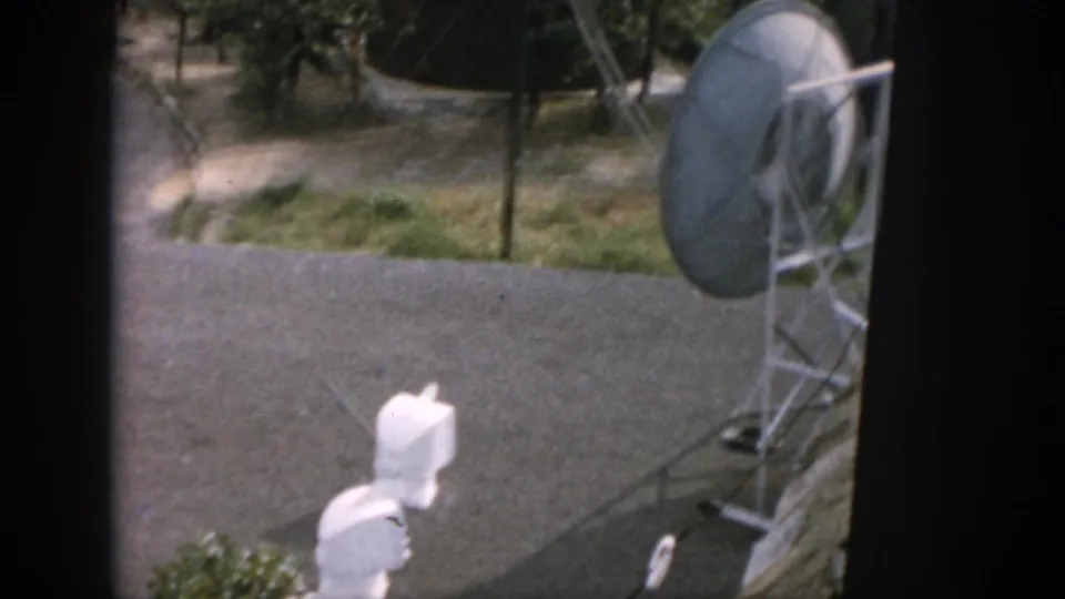 1958 Dayton view from a window toward a large dish-like antenna, white fixtures, paved ground, and trees.