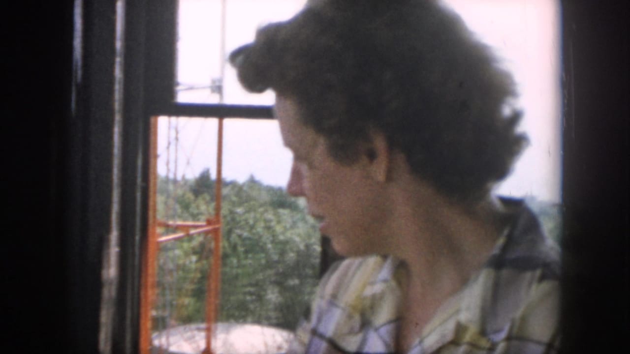 In 1958 Dayton-area home-movie footage, a girl in a plaid shirt looks out a window toward trees, hills, and utility poles.