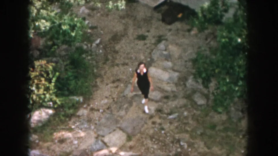 The girl continues along the rocky path through a green yard or hillside setting in 1958 Dayton-area home-movie footage.