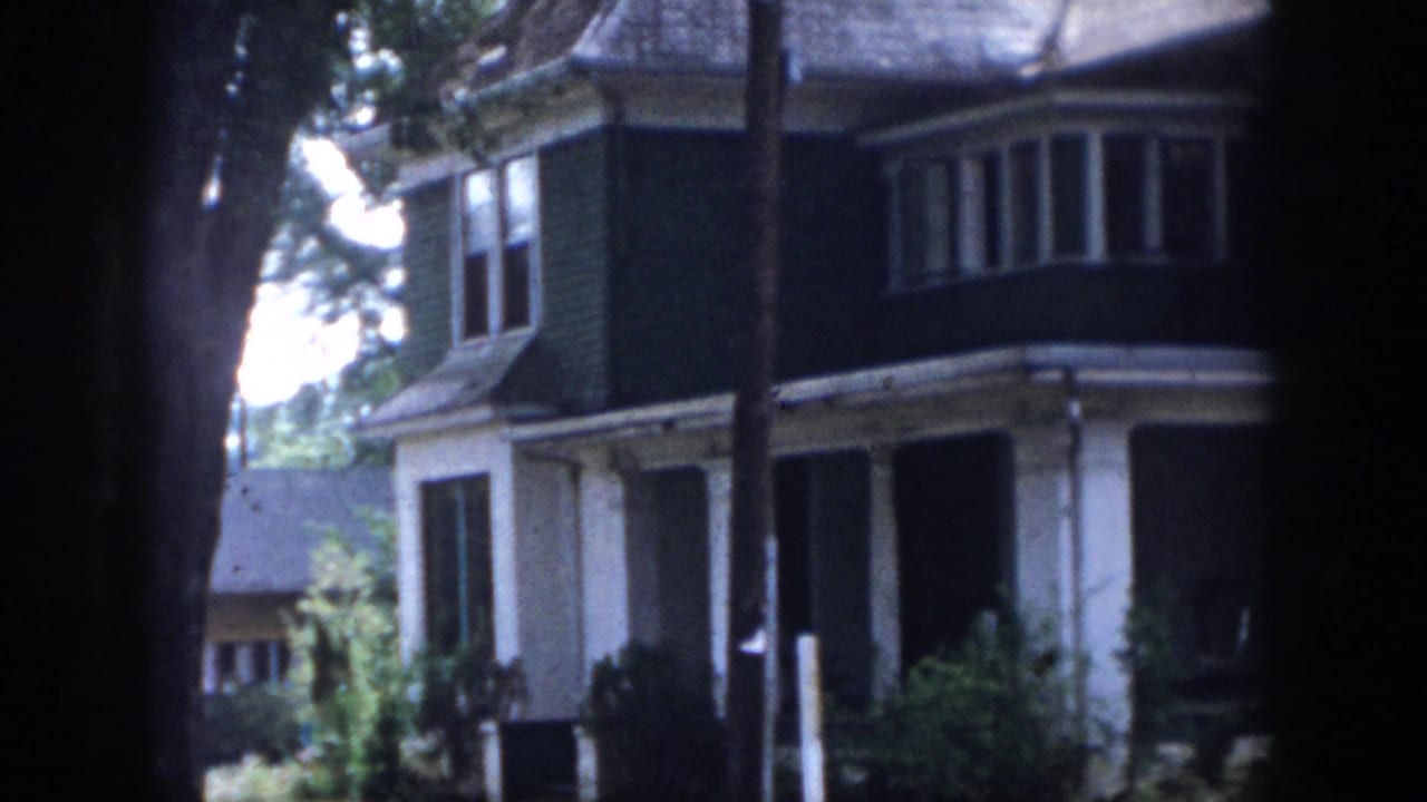 1958 Dayton, Ohio home-movie frame showing a two-story house with bay window, porch columns, dark siding, and trees in the foreground.