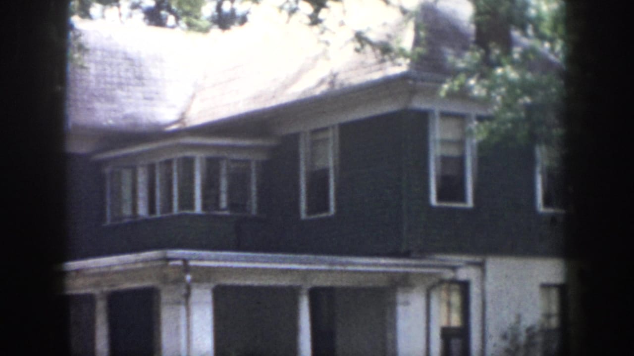 1958 Dayton residential exterior seen through dark foreground bands, showing the upper facade, bay window, white porch trim, and trees.