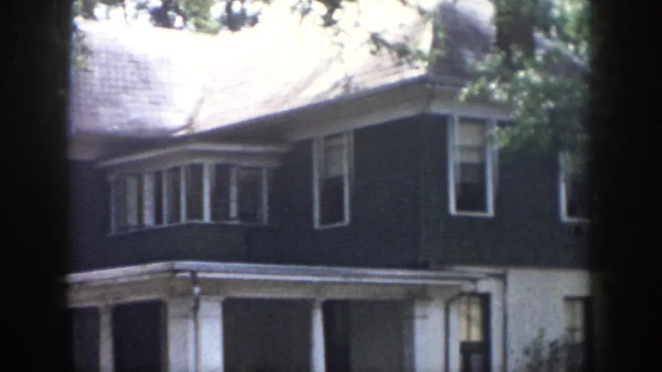 1958 Dayton residential exterior seen through dark foreground bands, showing the upper facade, bay window, white porch trim, and trees.