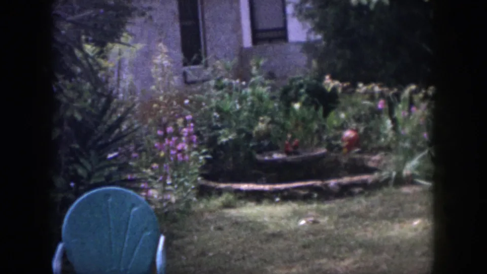 1958 Dayton backyard frame with a teal outdoor chair in the foreground and a planted garden bed near a house exterior.