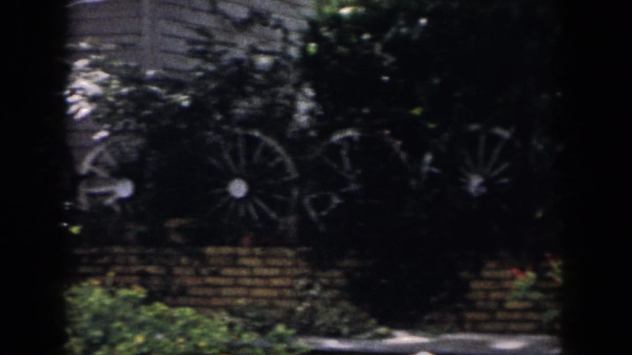 Dayton 1958 backyard view of decorative wagon wheels against brickwork and foliage, partly obscured by dark vignette.
