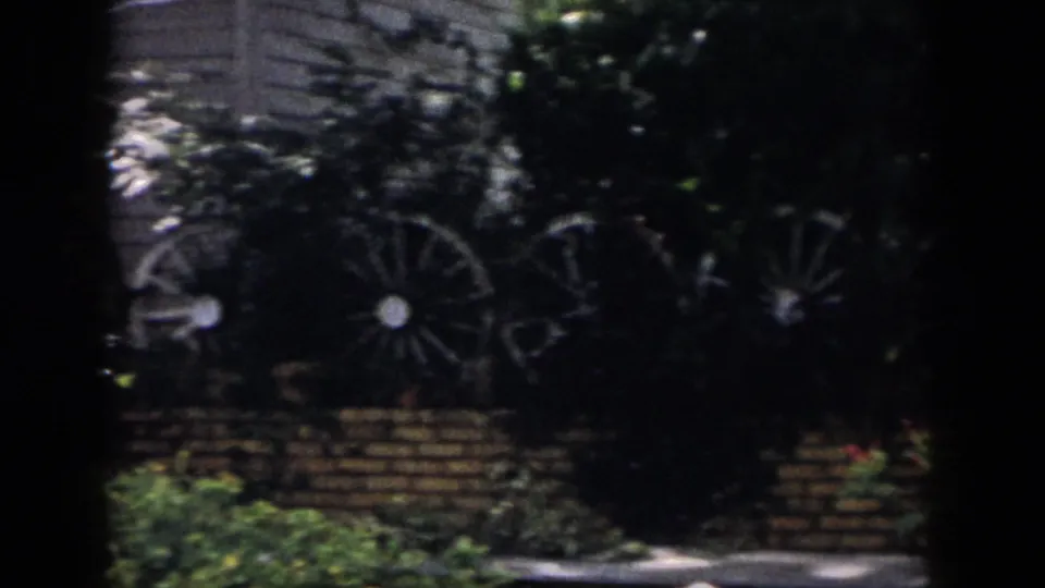 Dayton 1958 backyard view of decorative wagon wheels against brickwork and foliage, partly obscured by dark vignette.