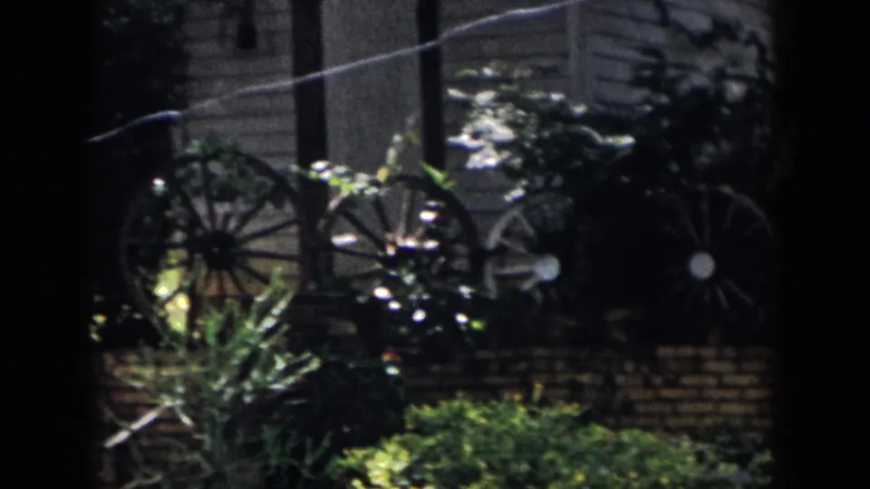 1958 Dayton backyard frame with wagon wheels, brickwork, shrubs, and a dark 8mm frame edge.