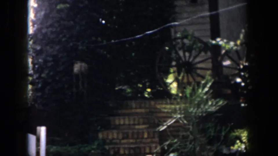 Dayton 1958 home-movie still of a planted backyard corner with wagon wheel ornamentation and brick steps.