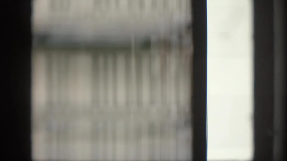 Blurred 8mm frame showing vertical window or screen lines, pale light, and dark film or structural edges.