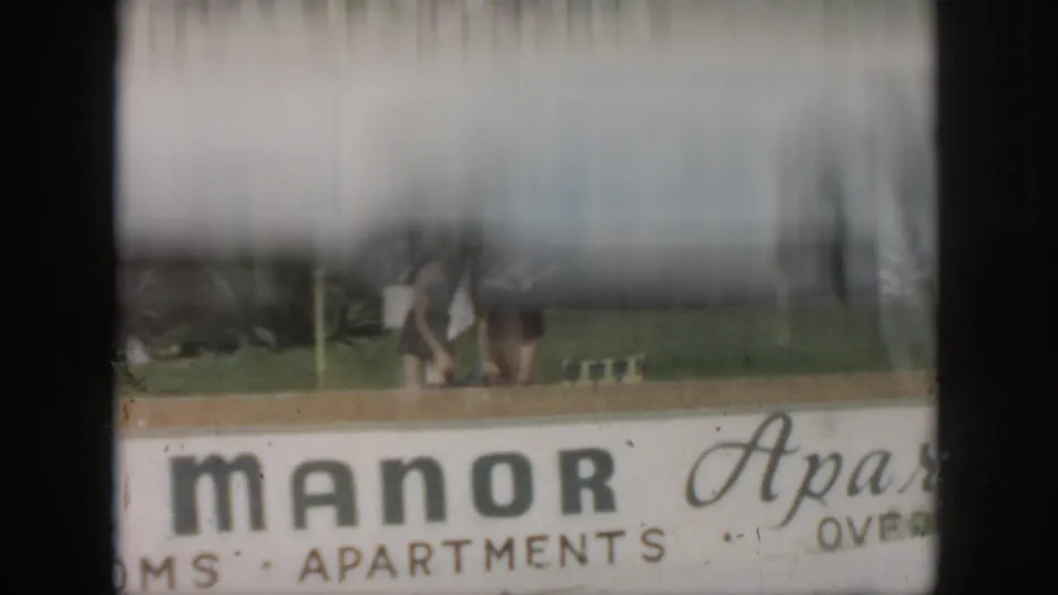 1958 New Orleans frame with the View Manor sign, partially obscured people, lawn, palms, and a bright horizontal film band.