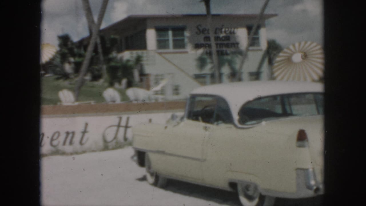 1958 New Orleans frame of a cream classic car parked by the Sea View Motor Inn exterior with palms and sunburst decor.