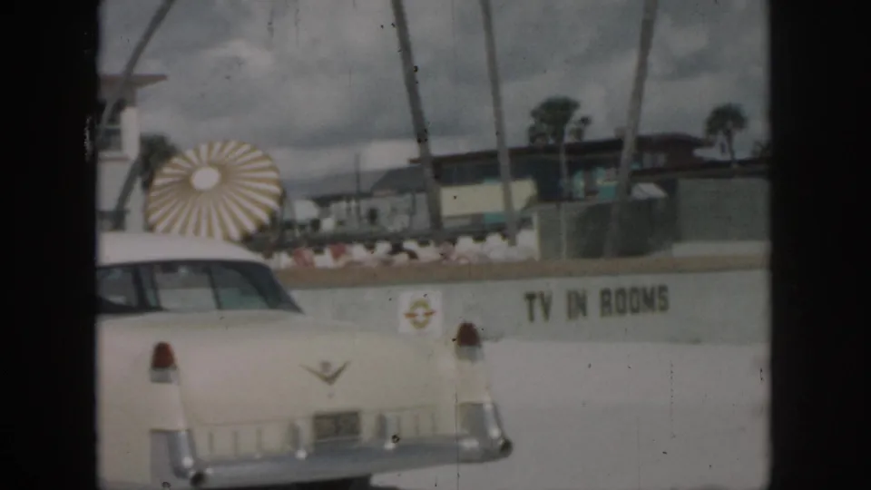 1958 New Orleans frame showing the car's rear near motel wall text advertising TV in rooms and a sunburst sign feature.