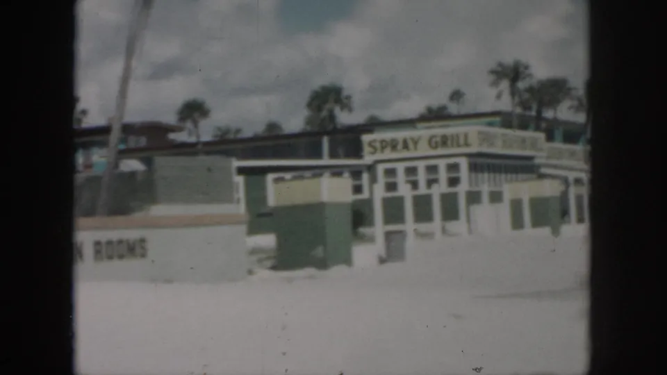 1958 New Orleans roadside frame with Spray Grill signage, a TV in Rooms sign, palm trees, and low commercial buildings.