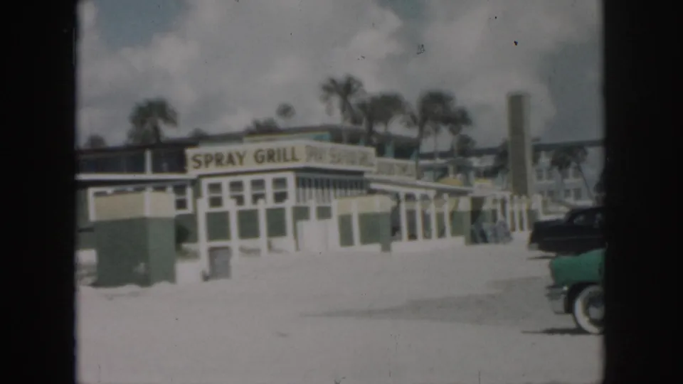1958 New Orleans view of the Spray Grill exterior, palm trees, a tall sign structure, and mid-century cars parked along the street.