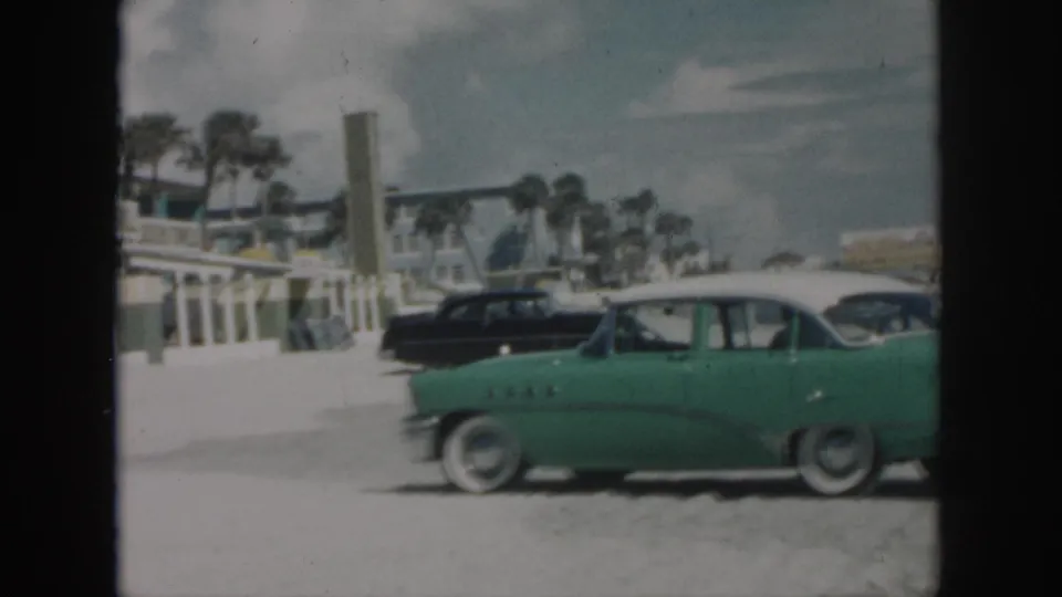 1958 New Orleans home-movie frame showing a green classic car with white roof beside a black sedan on sandy beachside ground.