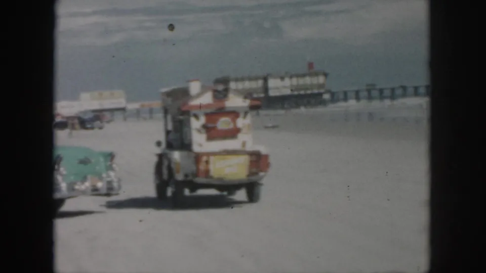 1958 New Orleans beach footage showing a turquoise car, a small truck, sand, surf, and a long pier in the background.
