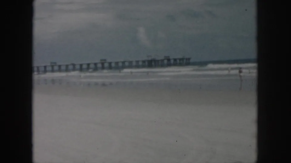 1958 New Orleans beach footage ending on the long pier, sand, low surf, and open sky after the truck has moved away.