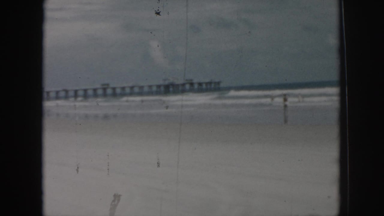 1958 New Orleans beach footage showing a long pier, pale surf, overcast sky, and a distant bather on the sand.