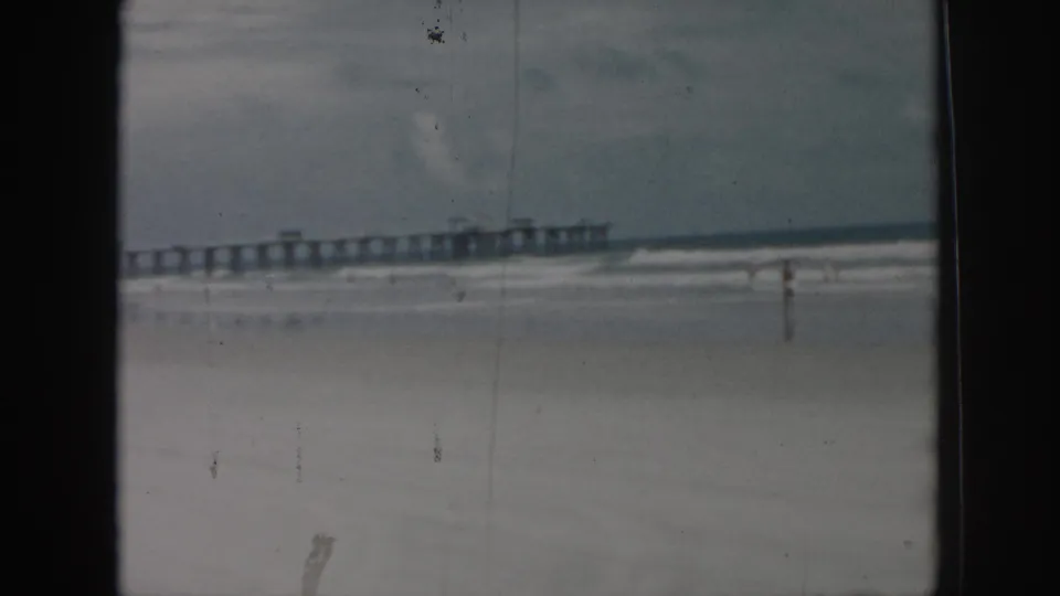 1958 New Orleans beach footage showing a long pier, pale surf, overcast sky, and a distant bather on the sand.
