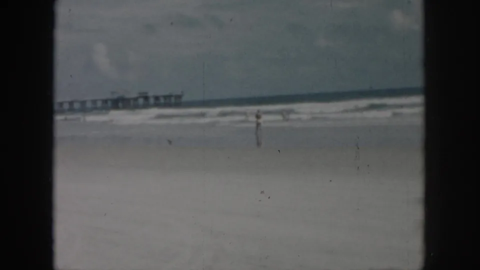 1958 New Orleans shoreline view with a distant pier, breaking waves, and one small figure near the waterline.