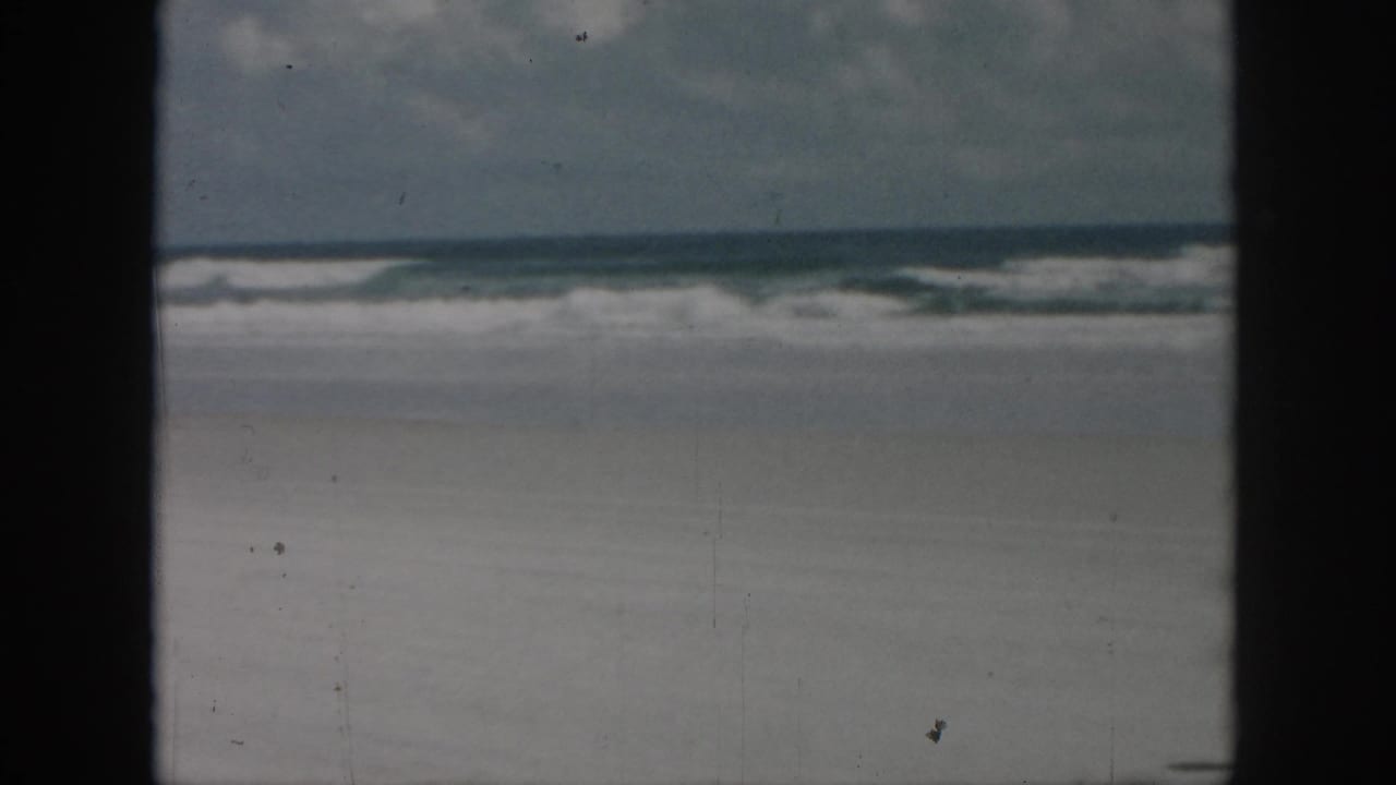 Wide beach view with waves, sky, and dark frame edges, with no person clearly visible.