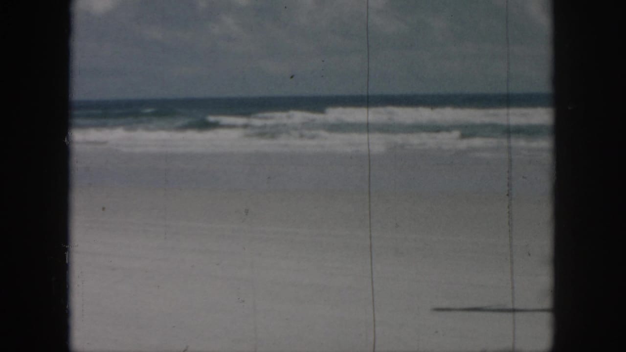 Sandy beach and ocean waves with a partial shadow or figure edge near the lower right.