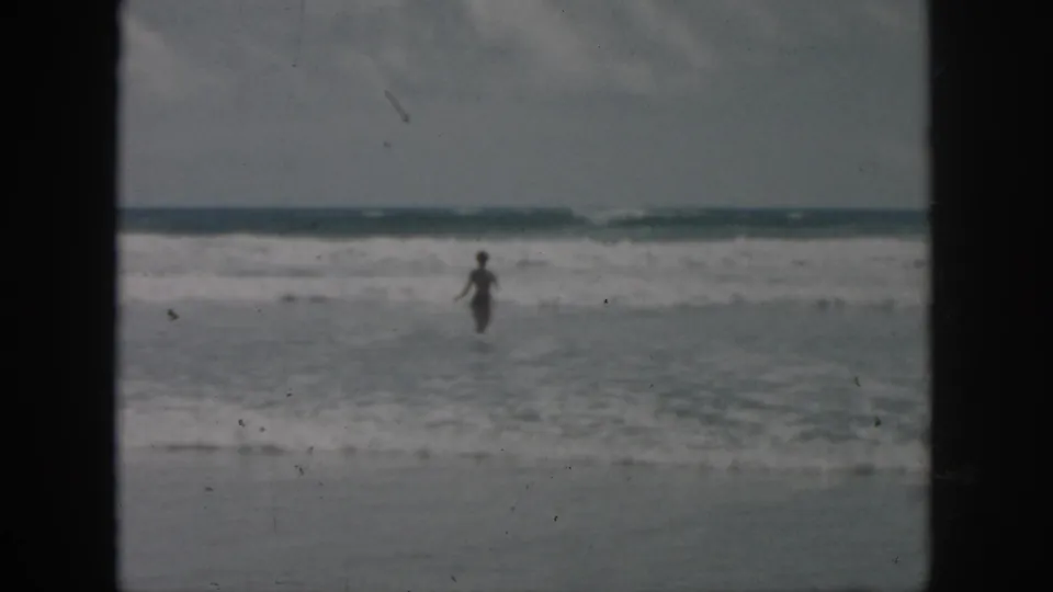 Distant figure wades through shallow beach water in a soft, grainy 1958 8mm frame associated with New Orleans, Louisiana.