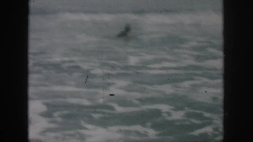 1958 8mm frame showing turbulent surf and a small distant swimmer in the ocean near New Orleans.