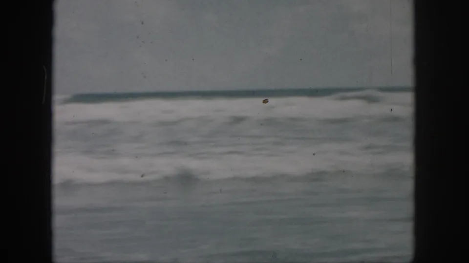 1958 8mm frame of rough ocean surf near New Orleans, with a low horizon and softened home-movie exposure.