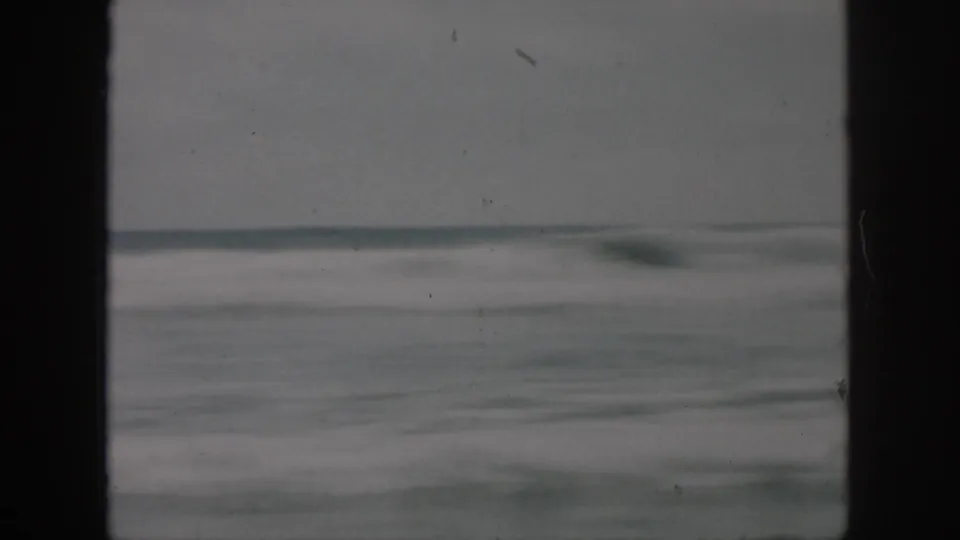 Soft 8mm view of ocean waves and a low horizon, with a heavy vertical border and visible film wear.