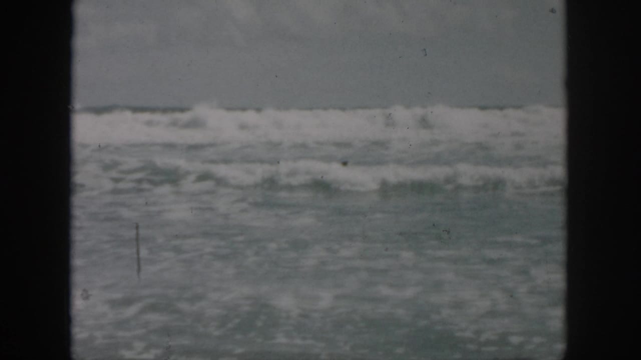 1958 8mm home-movie frame showing rough ocean surf near New Orleans, Louisiana, with no clear figures in the water.