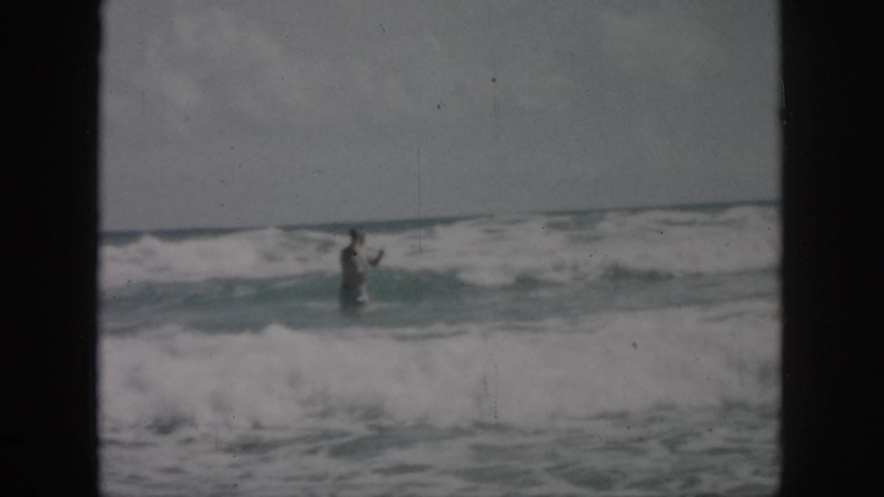 A distant swimmer stands or moves in foamy ocean waves.