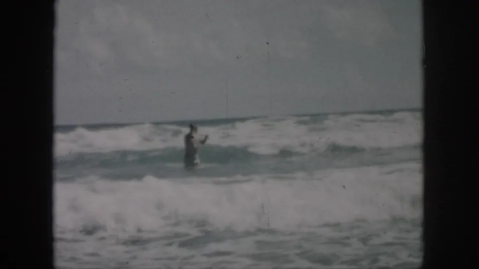 1958 8mm frame of a person in rough surf off the New Orleans, Louisiana coast, seen at a distance through soft focus.