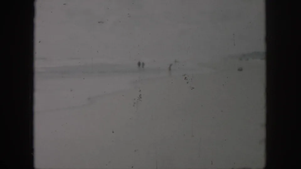 Wide 1958 8mm beach view near New Orleans, Louisiana, showing small distant figures on wet sand with waves in the background.