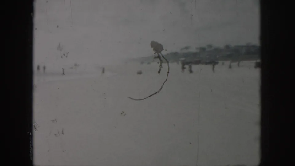 Soft 1958 New Orleans-area beach view with tiny figures, distant waterfront structures, dark frame edges, and surface wear.
