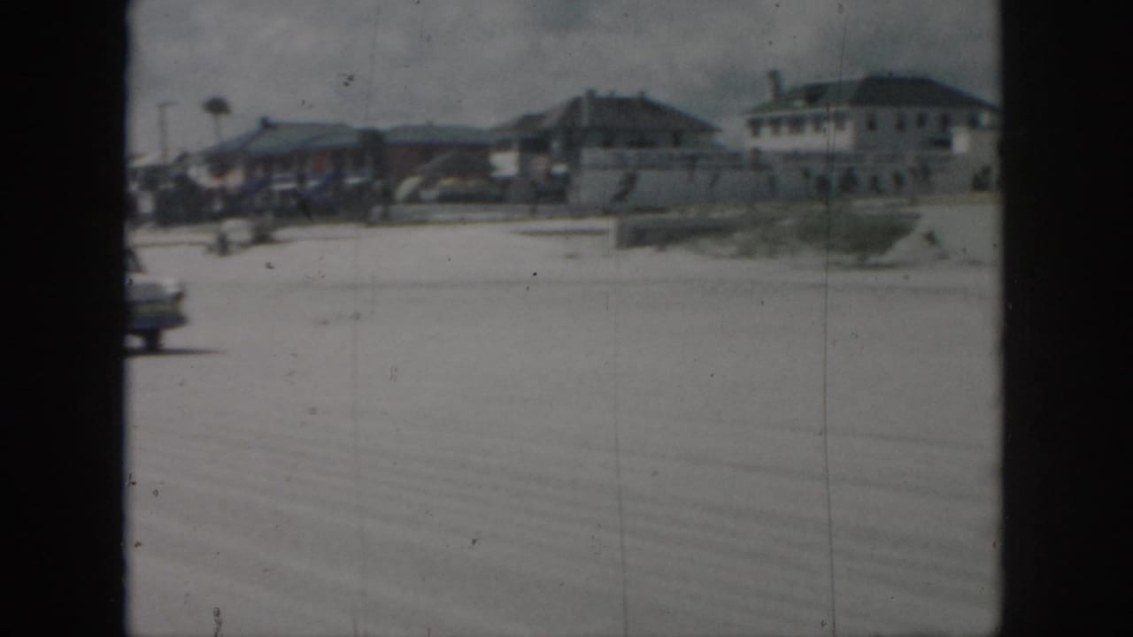 A broad roadway and distant buildings are seen through dark vertical film-frame edges.