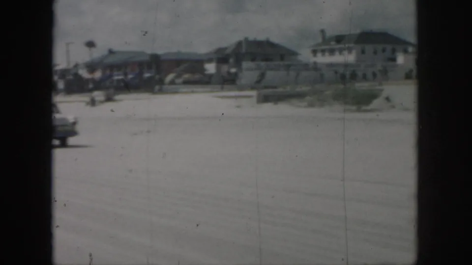 Soft 8mm view of a New Orleans roadway in 1958, with distant low buildings and partial passing traffic.