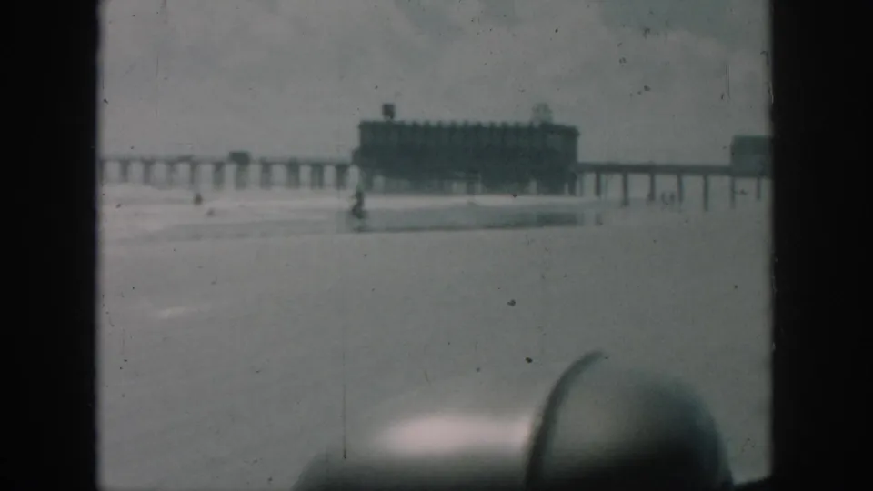 1958 New Orleans frame showing a distant pier and ocean surf from a soft, handheld 8mm beachside viewpoint.