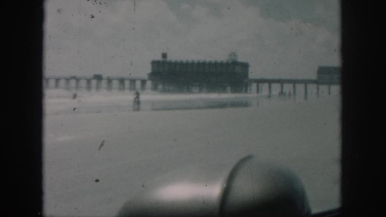 1958 8mm New Orleans travel frame showing a long pier and end building from inside a vehicle, with soft focus and foreground car interior.
