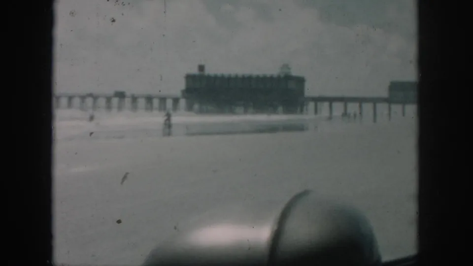 1958 8mm New Orleans travel frame showing a long pier and end building from inside a vehicle, with soft focus and foreground car interior.