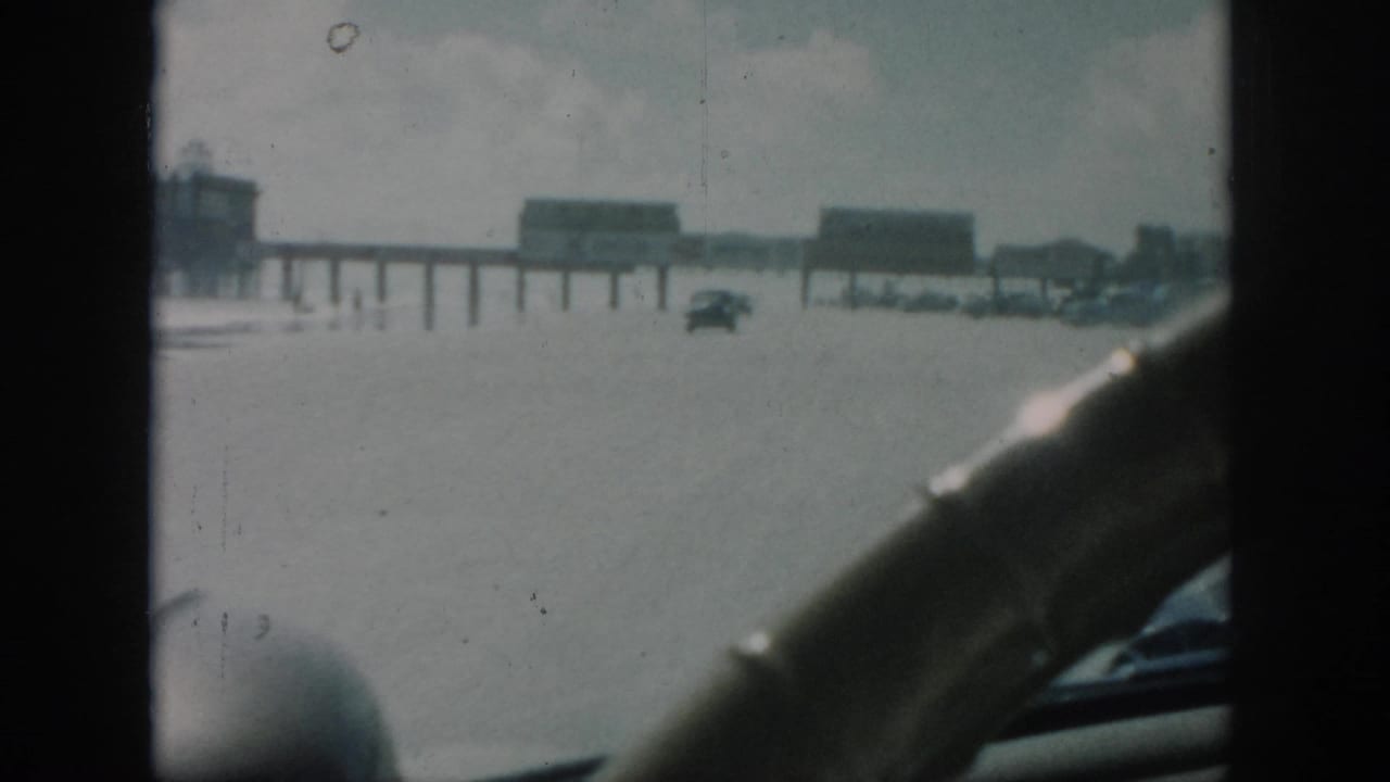 1958 New Orleans home-movie view from inside a car approaching a flooded road with distant cars and elevated structures.