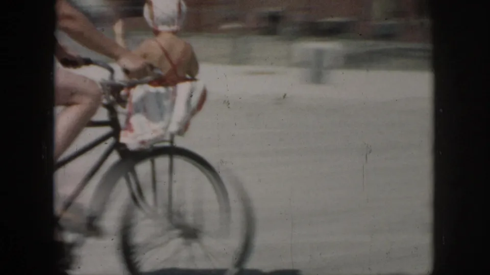 A blurred close view shows a bicycle rider passing near the camera, with a rear child seat or carrier visible but no clear face.