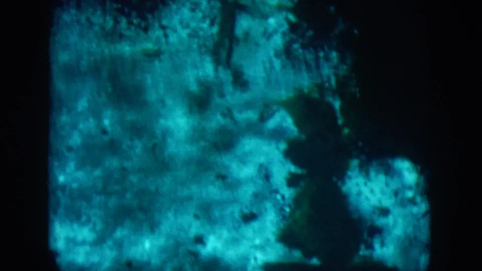 1958 8mm frame from New Orleans metadata showing murky blue-green water, dark shadows, and soft rock-like shapes.