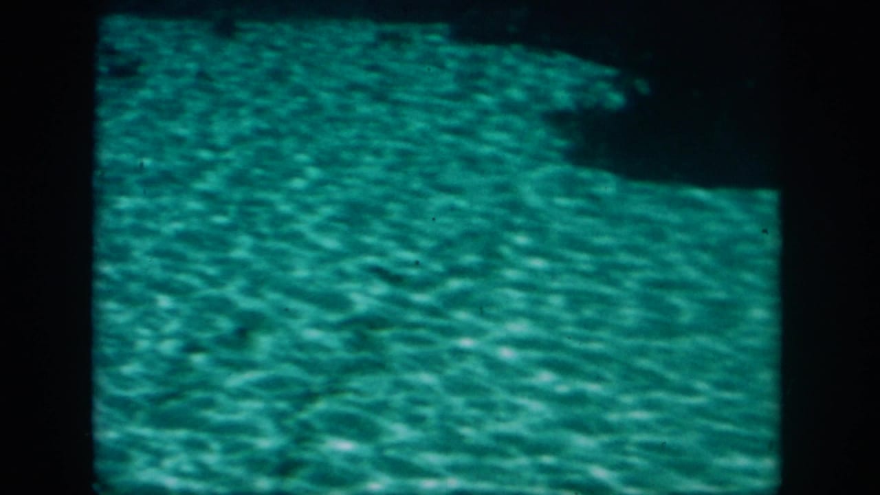 Archival 8mm frame from the New Orleans boat-tour clip showing green-blue water and a textured underwater bottom.